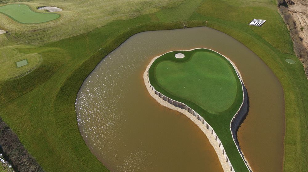 Edmonton Aerial view of a vibrant green synthetic grass island in a natural pond on a golf course